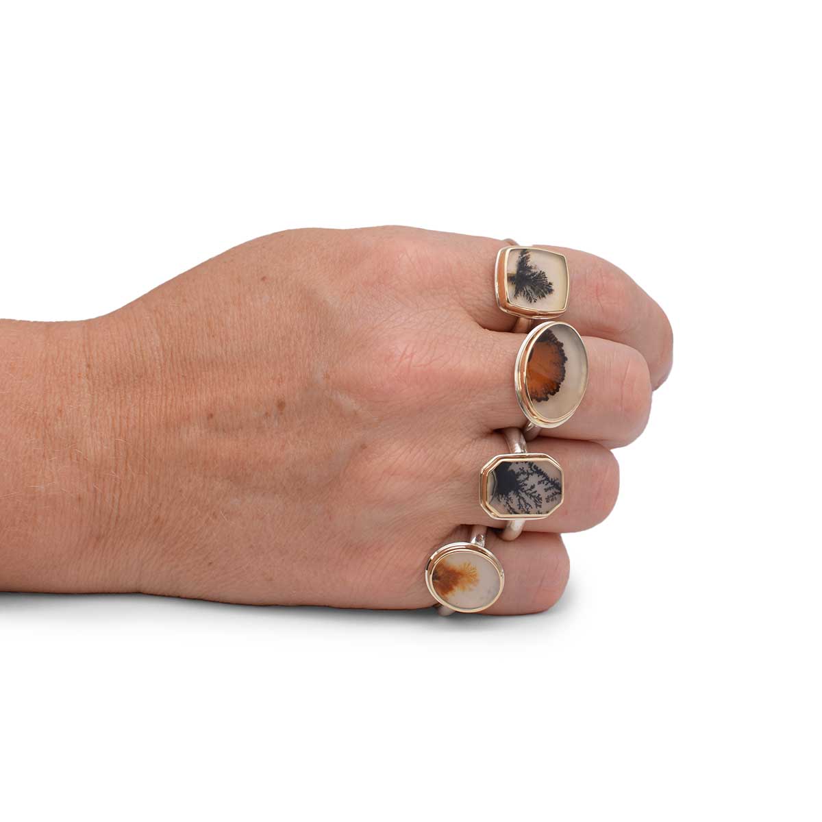 Hand wearing three gold rings with stone inlays on a white background