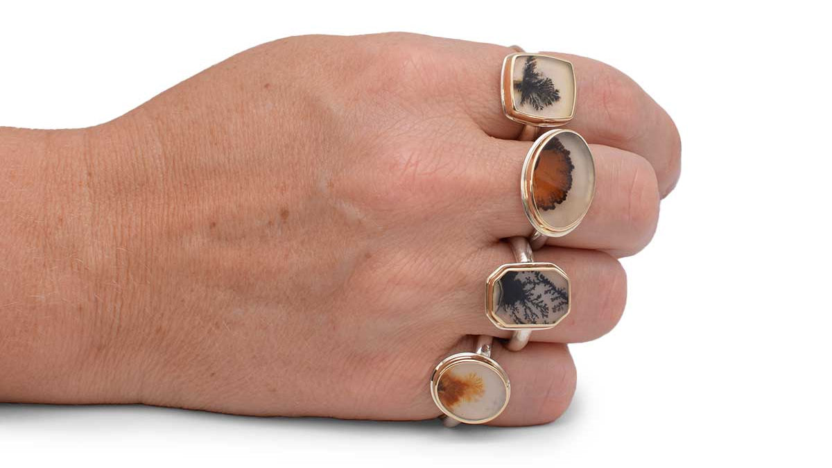 Hand wearing three gold rings with stone inlays on a white background