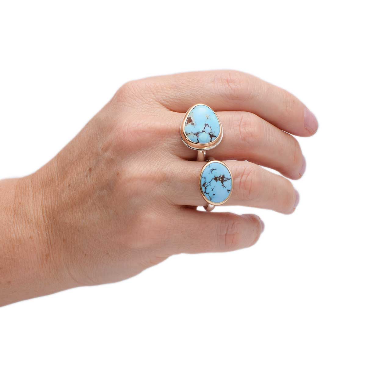 Hand wearing two turquoise stone rings on a white background